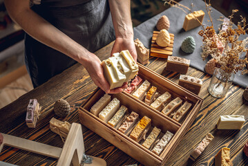 A woman soap maker holds handmade soap in her hands. A lot of different sliced pieces in a wooden box. Eco-friendly natural handmade cosmetics