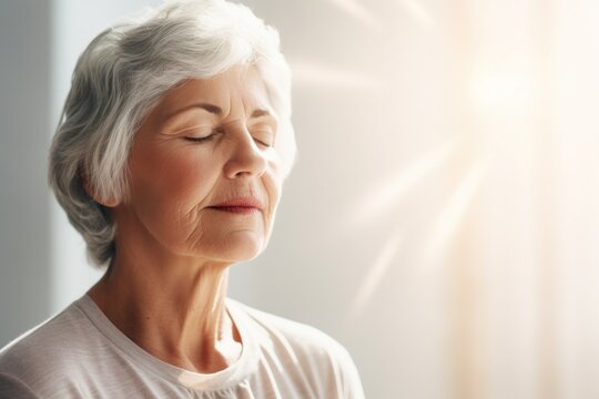 Serene mature woman enjoys peaceful moment, basking in warm sunlight indoors, wellness and serenity.