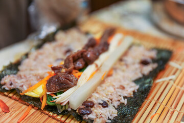kimbap making, a cherished Korean culinary tradition. Skilled hands roll rice, vegetables, and seaweed, crafting delicious, nutritious bites for an authentic dining experience