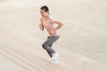 Fototapeta premium Full length sporty young Asian woman running on steps. Young female in sportswear jogging while exercising on the steps outdoor.