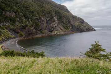 The view of blue water in Cedar Cove Newfoundland surrounded by cliffs with green vegetation
