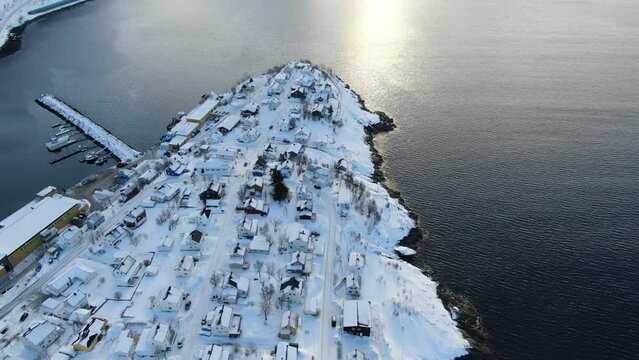 Drone view on the Tromso mountains in winter full of snow circling around Husoy, a small town on an island surrounded by the sea