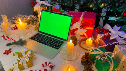 Festive New Year's table with a laptop with a chroma key on the screen. Colorful gift boxes,...