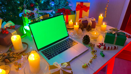 Beautiful Christmas table with a laptop with a green screen, New Year's gifts, burning candles, fir...