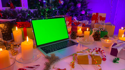 Laptop with a chroma key on the screen is on the New Year's table. Beautifully packaged gift boxes,...