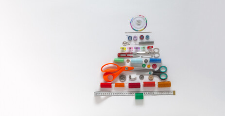 Merry Christmas. Unusual funny Christmas tree made from sewing and craft supplies on white background. Happy New Year greetings to people involved in sewing. Flat lay, closeup, top view, copy space
