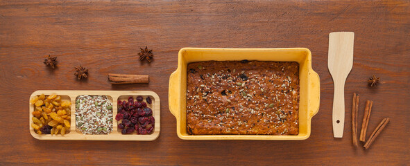 Top view of freshly baked homemade pie with raisins, cinnamon, sesame seeds and dry cranberries in ceramic baking dish on wooden table. Homemade holiday recipe for festive treats. Flat lay, copy space