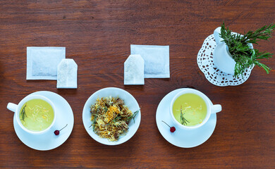 Rustic still life with two cups of hot herbal tea with chamomile, calendula and rosemary. Traditional treatment for colds. Green herbal tea in paper filter bags and bowl with dry calendula flowers