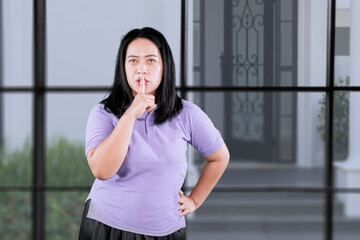 Fototapeta na wymiar Young secret chubby overweight fat woman wearing purple t-shirt casual clothes say hush be quiet