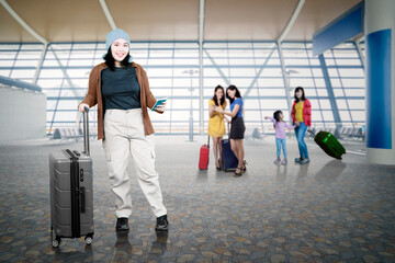 Full body front view young Asian female traveler with big smile carrying suitcase in airport