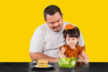 Cute little girl with father chooses a bowl of salad over hamburger
