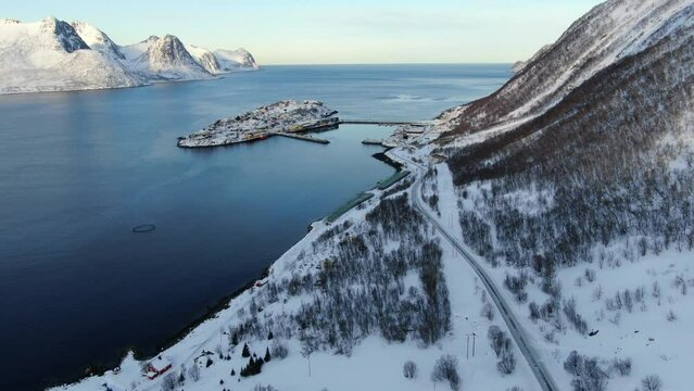 Drone view on the Tromso mountains in winter full of snow showing Husoy a small town on an island surrounded by the sea and its small port with flying seagulls