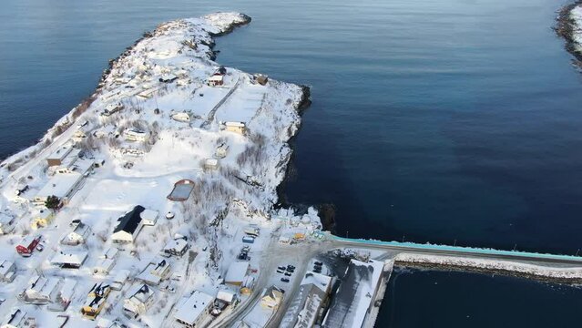 Drone view on the Tromso mountains in winter full of snow showing Husoy a small town on an island surrounded by the sea and its small port with flying seagulls