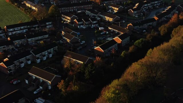 British neighbourhood housing aerial view looking down over early morning sunrise autumn coloured rooftops and gardens