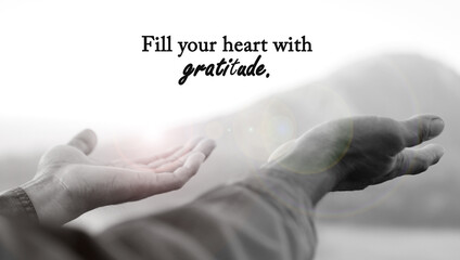 Grateful inspirational quote - Fill your heart with gratitude. With light on an open hands of person in black and white abstract art background. Thanksgiving and spirituality concept.
