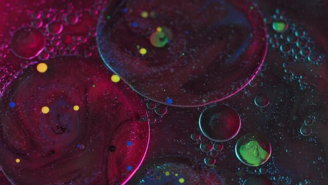 Abstract background. Paint glitter bubbles. Sparkling mix. Purple red yellow liquid ink round spots floating on shiny water surface in magic art.
