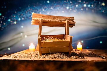Small wooden manger filled with straw, on snow and candles around and a blue sky.