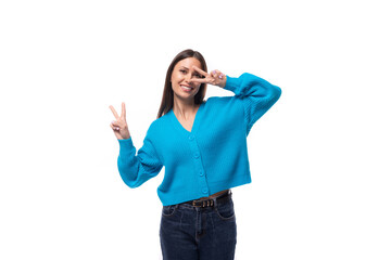 Obraz na płótnie Canvas young positive pretty caucasian woman with black hair is dressed in a stylish blue cardigan and jeans on a white background