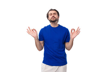 young brunette man with a beard dressed in a blue t-shirt meditates on a white background