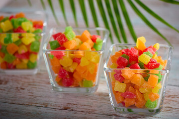 Healthy sweet snack of candied fruits in a glass dish on a wooden table. Small transparent vases are filled with colorful delicious candied fruits. 