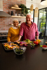 Happy caucasian senior couple at kitchen counter with fresh vegetables, copy space