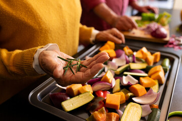 Midsection of senior caucasian couple preparing vegetables, seasoning with fresh rosemary