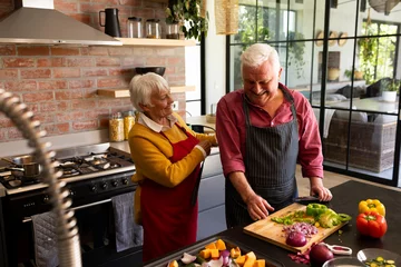  Happy caucasian senior couple preparing vegetables, putting on aprons in sunny kitchen © wavebreak3