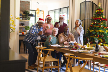 Happy diverse group of senior friends in santa hats celebrating and toasting at christmas dinner