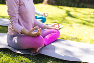 Low section of biracial lesbian couple practicing yoga meditation in sunny garden, copy space