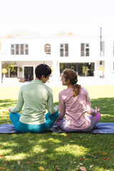 Happy biracial lesbian couple practicing yoga meditation sitting in sunny garden, copy space