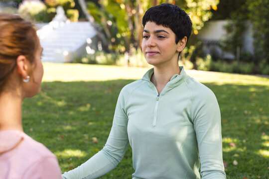 Happy biracial lesbian couple practicing yoga meditation sitting stretching in sunny garden