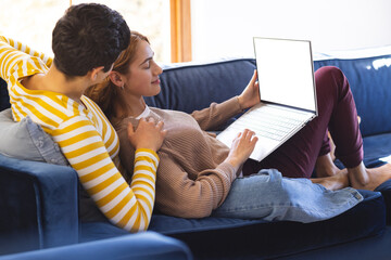 Happy biracial lesbian couple relaxing on couch using laptop together
