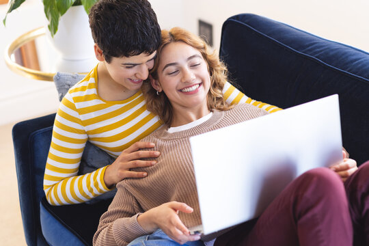 High angle of happy biracial lesbian couple relaxing on couch using laptop together