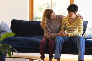 Sad biracial lesbian couple embracing and comforting, on couch in sunny living room, copy space - Powered by Adobe