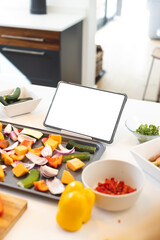 Chopped vegetables in backing tray and tablet with copy space screen on kitchen worktop, copy space