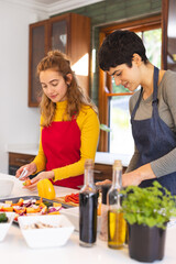 Focused biracial lesbian couple peeling and chopping vegetables in kitchen, copy space