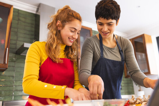 Happy biracial lesbian couple using tablet preparing vegetables in kitchen - Powered by Adobe