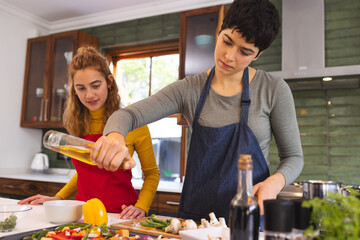 Focused biracial lesbian couple cooking, drizzling oil on chopped vegetables in kitchen at home