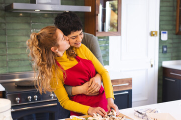 Happy biracial lesbian couple chopping vegetables and embracing in kitchen, copy space