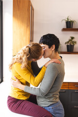 Romantic biracial lesbian couple embracing and kissing in kitchen, copy space