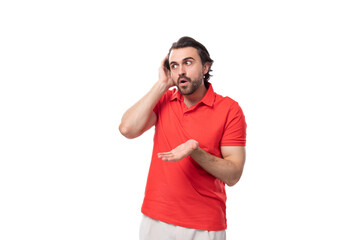 young handsome man with black hair and beard dressed in a red t-shirt throws up his hands using a smartphone