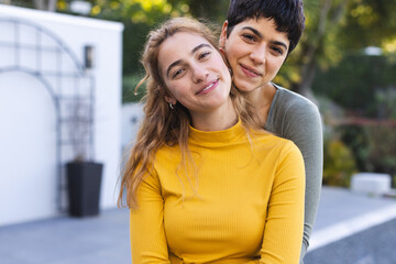 Portrait of happy biracial lesbian couple standing on garden terrace embracing and smiling