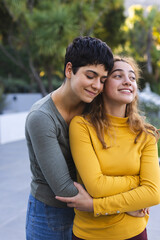 Happy biracial lesbian couple standing on garden terrace embracing and smiling