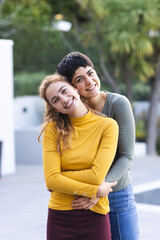 Portrait of biracial lesbian couple standing on garden terrace embracing and smiling, copy space