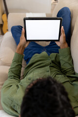 Biracial man lying on sofa using tablet with copy space on screen at home
