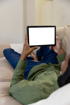 Biracial man lying on sofa using tablet with copy space on screen at home
