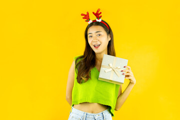 pretty asian woman with reindeer headband holding gift box isolated on yellow background, christmas...