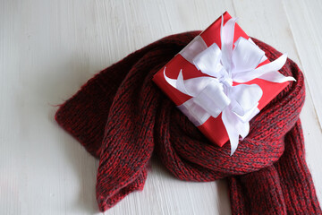 Red gift box isolated on a red knitted scarf with white wooden background with. Christmas's day concept. Planning scheduling agenda, Event, organiser x'mas day. Flat lay, top view.