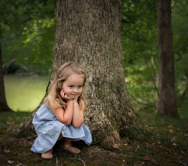 Beautiful little girl crouching with hands on cheeks outdoors