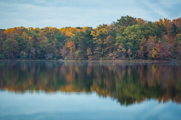Changing fall leaves on lakeshore with reflection in water.